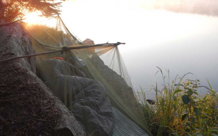 A person rests in a sleeping back on a cliff above a body of water.